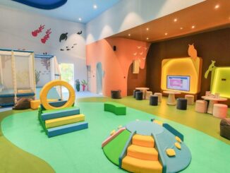 Красочная крытая игровая площадка для детей с конструкциями из пенопласта для лазания, кольцом, мягкими ступеньками и яркими фресками на стенах.
