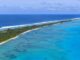 Aerial view of a turquoise lagoon with a white-sand barrier island lined by palm trees and the deep blue ocean beyond.