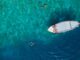 Aerial view of a white boat floating on turquoise sea with two snorkelers in the clear water nearby.