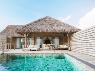 Thatched-roof bungalow villa with a wooden deck and turquoise pool in front, outdoor seating visible on the deck.